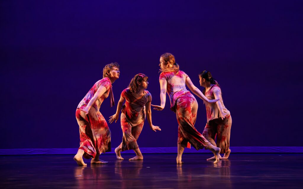 Four dancers face each other in a circle