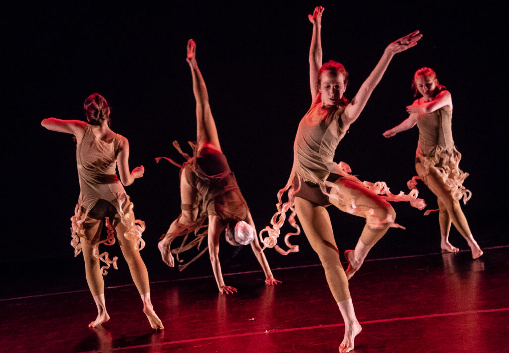 Four dancers wearing costumes with squiggly noodle skirts